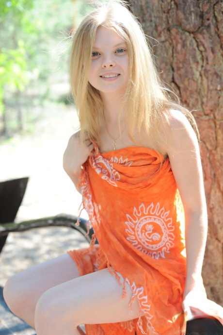 Young blonde Kisa removes her wrap to pose nude on bench under an old tree 88553263